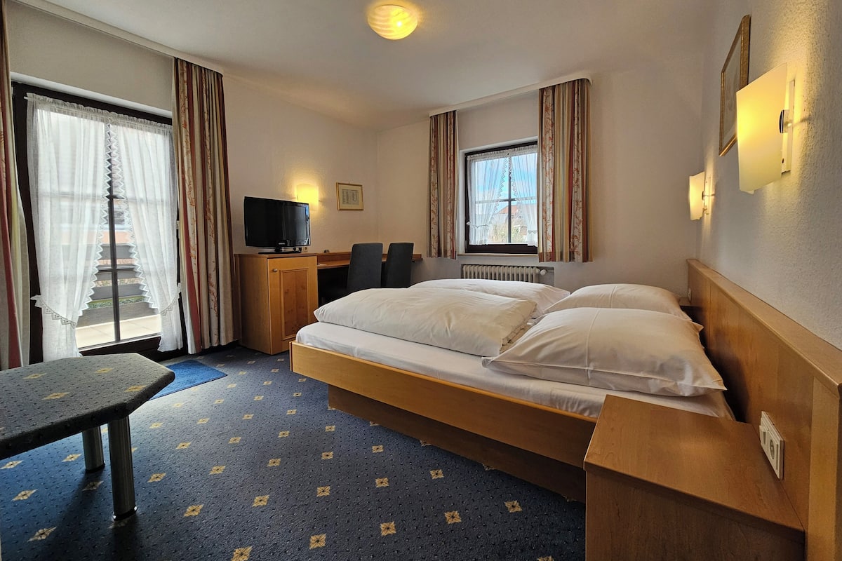 A hotel room with a bed, a desk with a computer, a television, and a window with curtains.