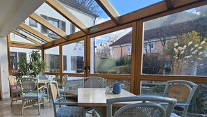 A sunlit room with a large glass window, a table with chairs, and a potted plant. - ARRIVEL Hotel am Bergson (Munich)