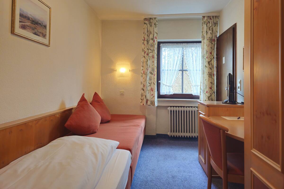 A hotel room with two beds, a desk, a mirror, a radiator, and a window with curtains.