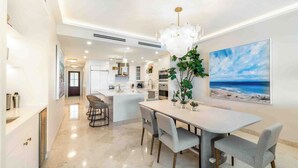 Une cuisine moderne avec des meubles blancs, un îlot central et un coin repas comprenant une table et des chaises.