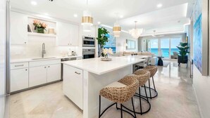 Une cuisine moderne avec des meubles blancs, un grand îlot central doté de tabourets et un éclairage suspendu.