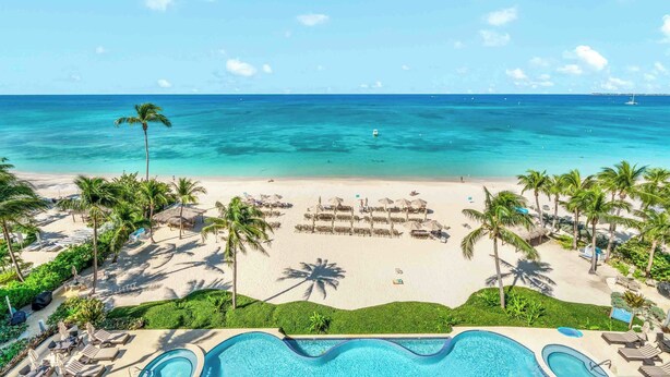 Un complexe hôtelier doté d’une piscine, d’une plage et de palmiers.