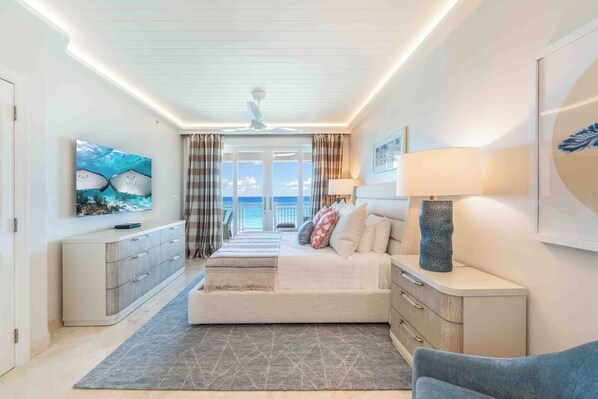Un dormitorio moderno con cama, mesitas de noche, televisión y vista al mar.