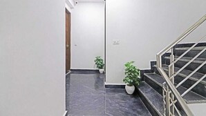 A hallway with a marble floor, a staircase with metal railings, and two potted plants. - Hotel Vijaydeep Place Near Delhi Airport (New Delhi)