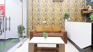 A reception area with a patterned wallpaper, a brown sofa, a white table, and a potted plant. - Hotel Vijaydeep Place Near Delhi Airport (New Delhi)