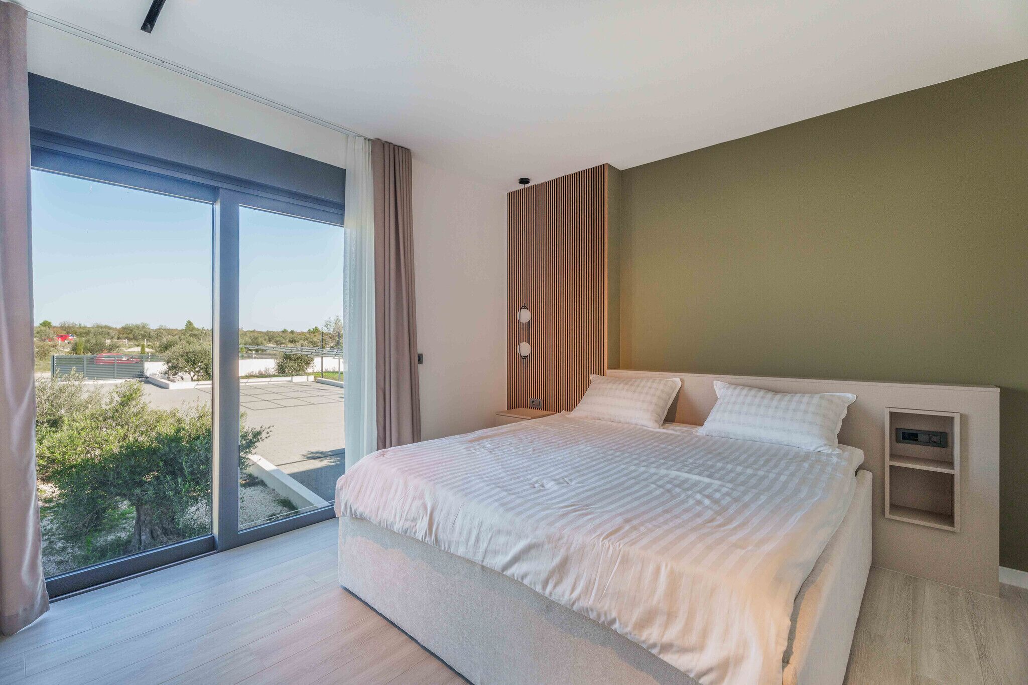 Une chambre moderne avec un grand lit, une table de chevet et une vue sur l’extérieur grâce à une porte-fenêtre coulissante.