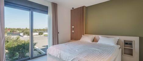 Une chambre moderne avec un grand lit, une table de chevet et une vue sur l’extérieur grâce à une porte-fenêtre coulissante.