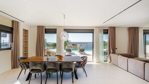 A modern living room with a large window, a dining area with a wooden table and chairs, and a sofa. - Villa Freedom (Vodice)