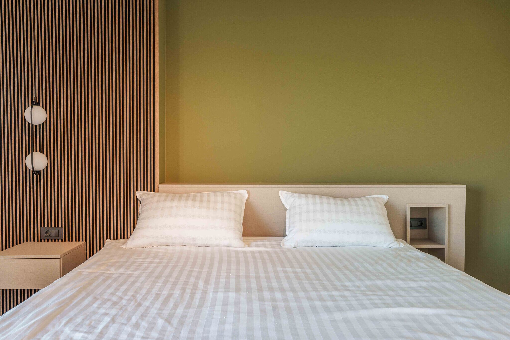 Un letto ben rifatto con due cuscini, un comodino e una piccola mensola con una radio.