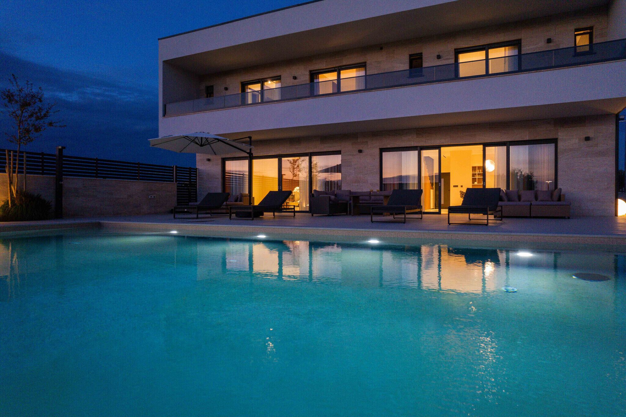 Una casa moderna de dos plantas con piscina, mobiliario exterior y ventanas amplias.