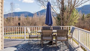 A deck with a table and chairs, overlooking a mountainous landscape.