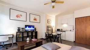 Quarto de hotel compacto com cama, escrivaninha, televisão e cozinha compacta.