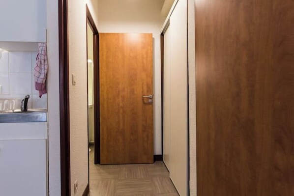 A narrow hallway with a wooden door at the end, a white tiled wall, and a small countertop with a cloth.