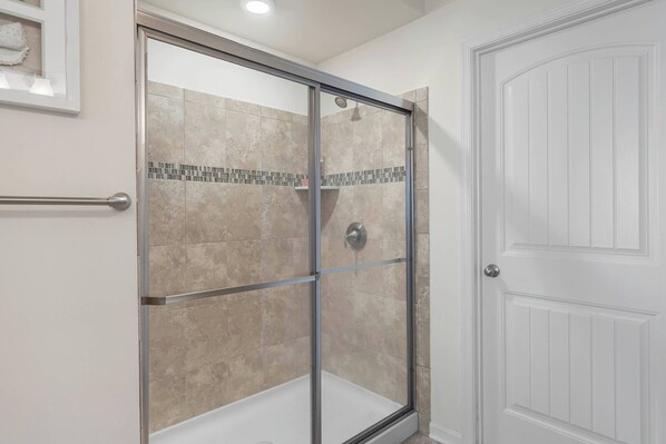 A shower with a glass door, beige tiles, and a white door next to it.