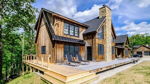 A wooden cabin with a stone chimney, a deck with lounge chairs, and a garage. - River access/Golf 2 miles/hiking/skiing/hot tub/sauna (Newry)
