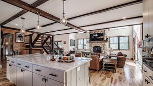 A spacious kitchen with a large island, wooden beams, and a stone fireplace. - River access/Golf 2 miles/hiking/skiing/hot tub/sauna (Newry)