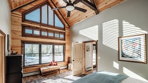 A spacious bedroom with a large window, a ceiling fan, and a bed with a patterned bedspread. - River access/Golf 2 miles/hiking/skiing/hot tub/sauna (Newry)