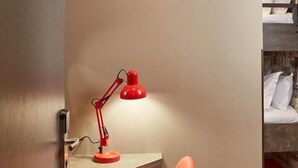 A hotel room with a red desk lamp, a red chair, a bunk bed, and a carpet with red and grey squares. - The Pierrooms (Oban)