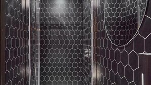 A modern bathroom with a glass-enclosed shower, a white pedestal sink, and hexagonal patterned walls. - The Pierrooms (Oban)