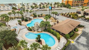 Un resort con una amplia piscina, vista a la playa y zona de estacionamiento.