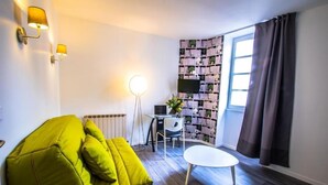 Una habitación con un sofá verde, una mesa redonda, una estantería y una ventana con cortinas.