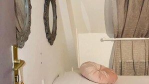 Un dormitorio con una cama, dos almohadas, una mesita de noche, un espejo y una cortina.