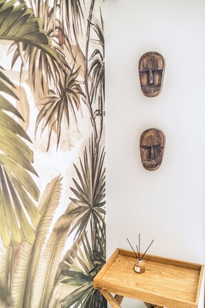 A room with a tropical-themed wallpaper, a wooden tray with a candle, and two wooden masks on the wall.