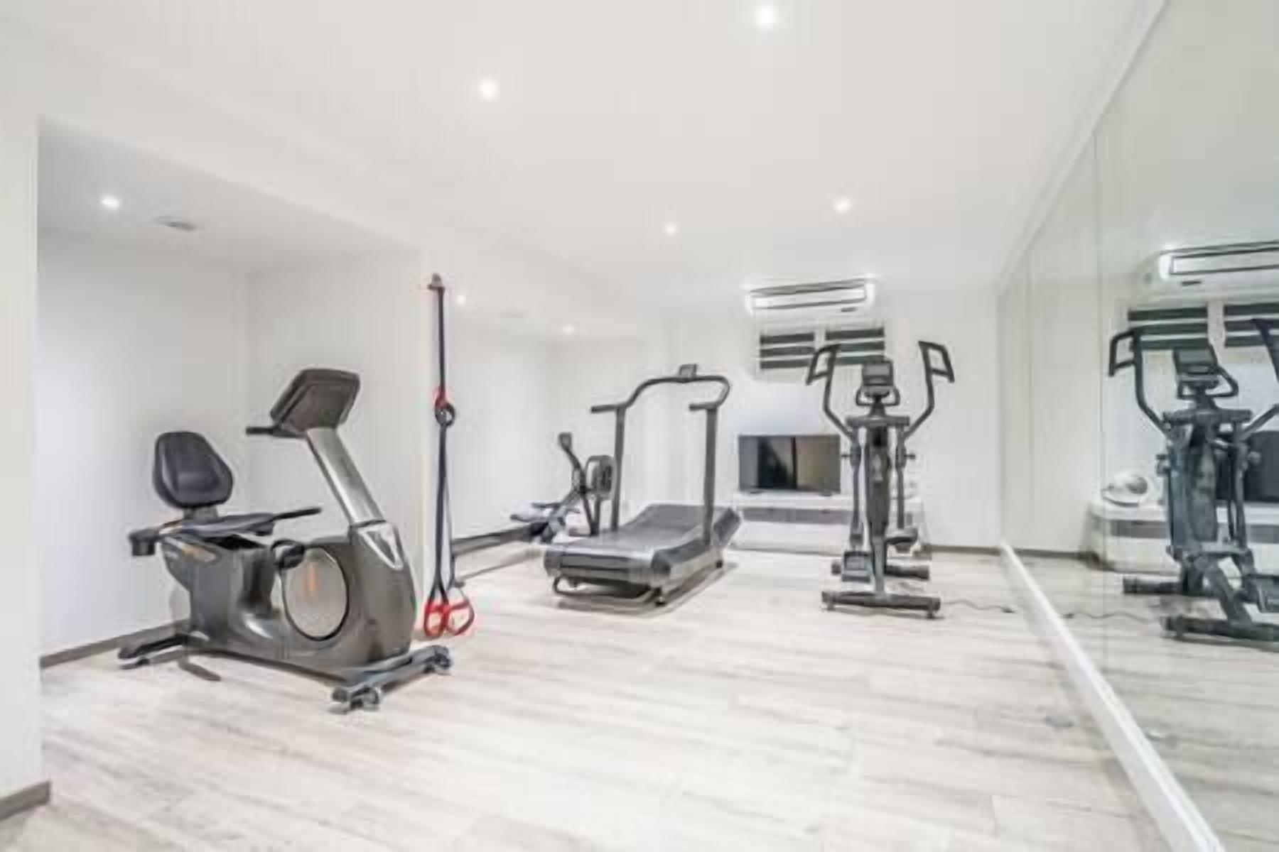 A modern gym with cardio machines, weight training equipment, and a mirrored wall.
