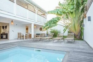 A poolside area with lounge chairs, a dining setup, and a large plant.