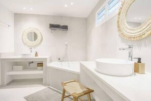 A modern bathroom with a round mirror, a freestanding stool, and a bathtub.