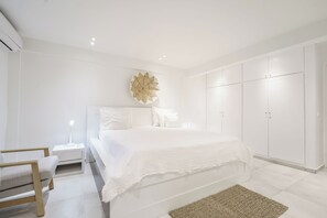 A modern bedroom with a large bed, white walls, and built-in wardrobes.