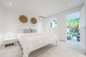 A bedroom with a large bed, bedside tables, and a view of the garden through an open door.