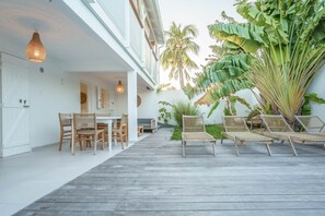 A covered outdoor patio with wooden flooring, wicker furniture, and hanging pendant lights.