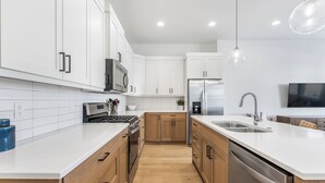 Une cuisine moderne avec des meubles blancs, des appareils électroménagers en acier inoxydable et un plancher en bois.