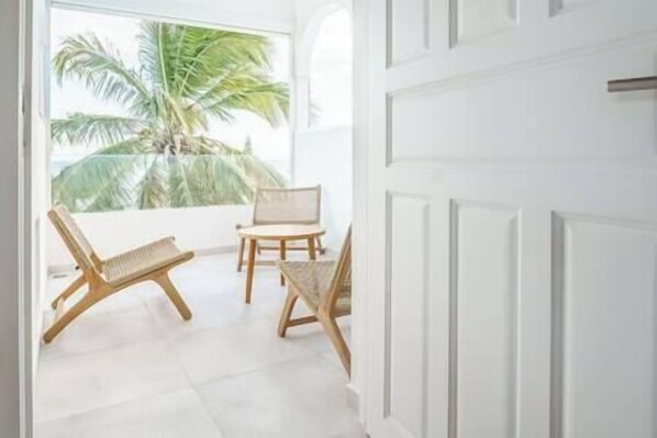 A room with a white door, a window with a view of palm trees, and two wooden chairs.
