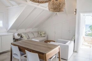 A modern kitchen with a wooden table and white chairs, a white sofa, and a hanging light fixture.