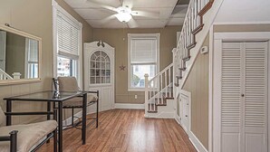 Une pièce avec une table en verre, deux chaises, un ventilateur de plafond, un escalier et une porte.
