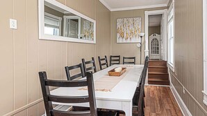 Une salle à manger avec une longue table, des chaises, un miroir et un escalier menant à une autre pièce.