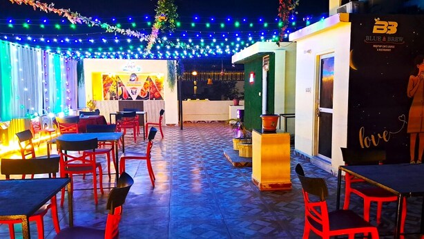 Un espace extérieur aménagé avec des tables et des chaises, une scène ornée d’une banderole et un panneau indiquant « BB Blue & Brew ».
