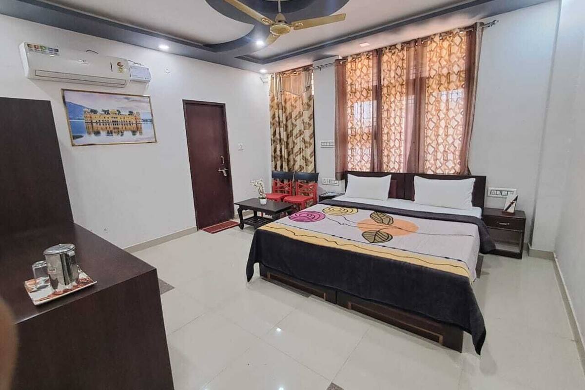 A hotel room with a bed, a desk, a chair, a ceiling fan, and a window with curtains.