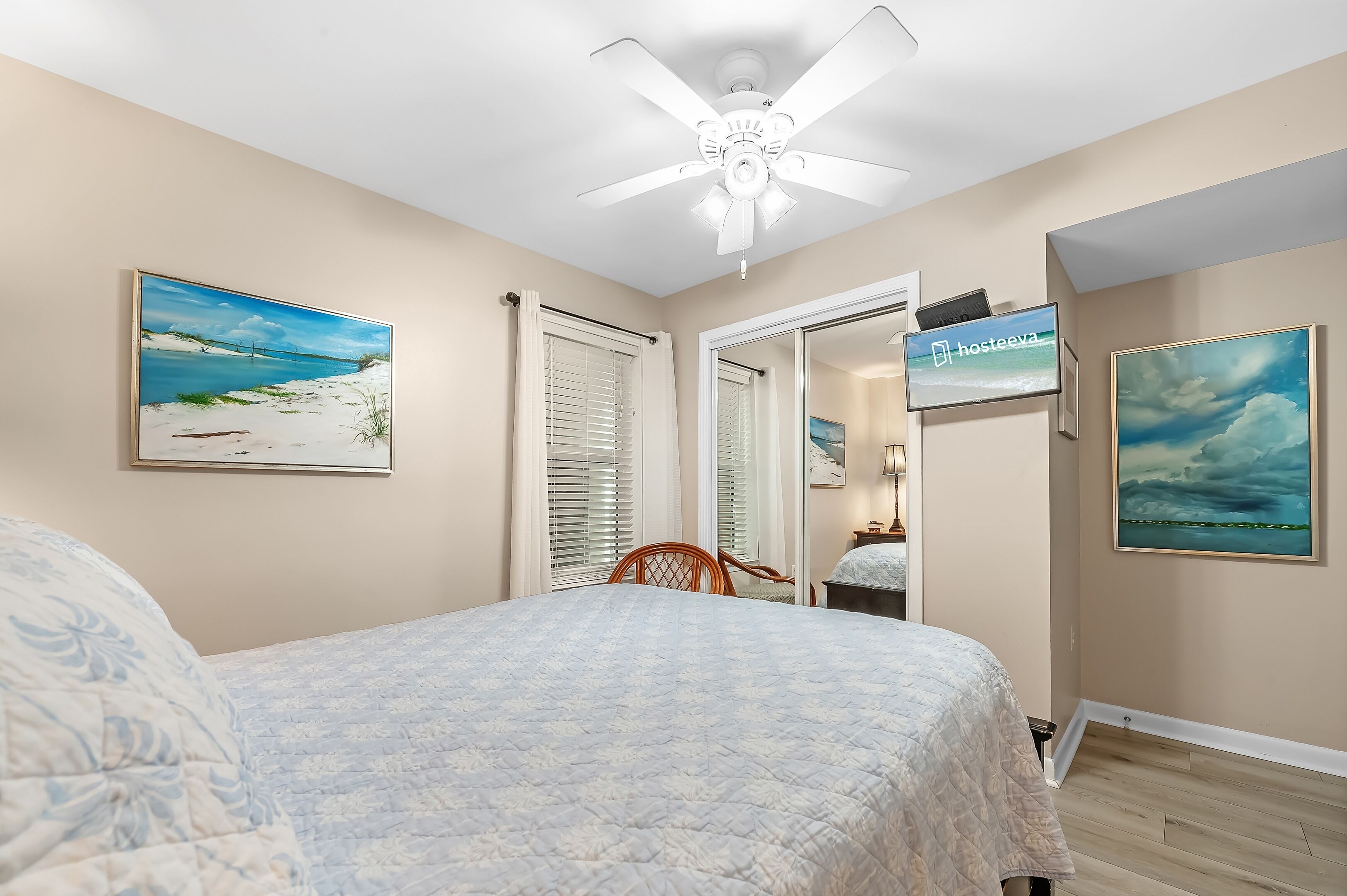 A bedroom with a bed, a ceiling fan, a TV, and artwork on the walls.