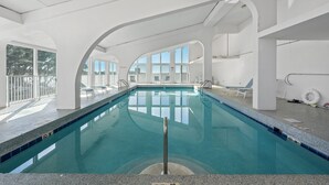 A swimming pool with clear blue water, surrounded by white walls and large windows. - Compass Point 508 (Gulf Shores)