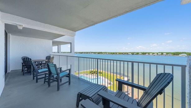 A balcony with chairs and a table, overlooking a body of water and a distant shoreline. - Compass Point 508 (Gulf Shores)