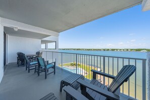 Un balcon avec des chaises et une table, donnant sur une étendue d’eau et une côte lointaine.