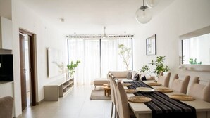 A modern dining area with a long table, cushioned chairs, and a central sofa.