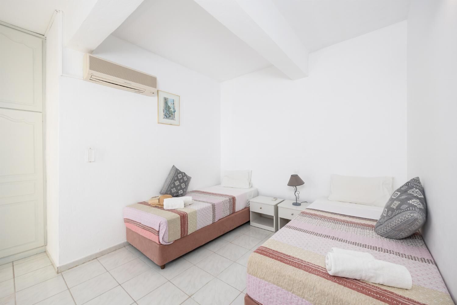 Une chambre avec deux lits, une table de chevet, une lampe et un tableau au mur.