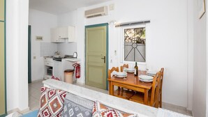 Cocina compacta con armarios blancos, microondas y extintor. Se encuentra una mesa de comedor con sillas cerca de una ventana con vistas a árboles.