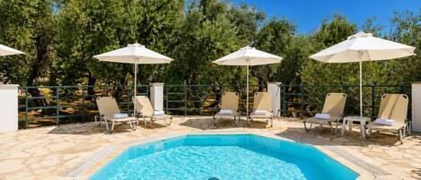 A swimming pool with lounge chairs and umbrellas, surrounded by trees.