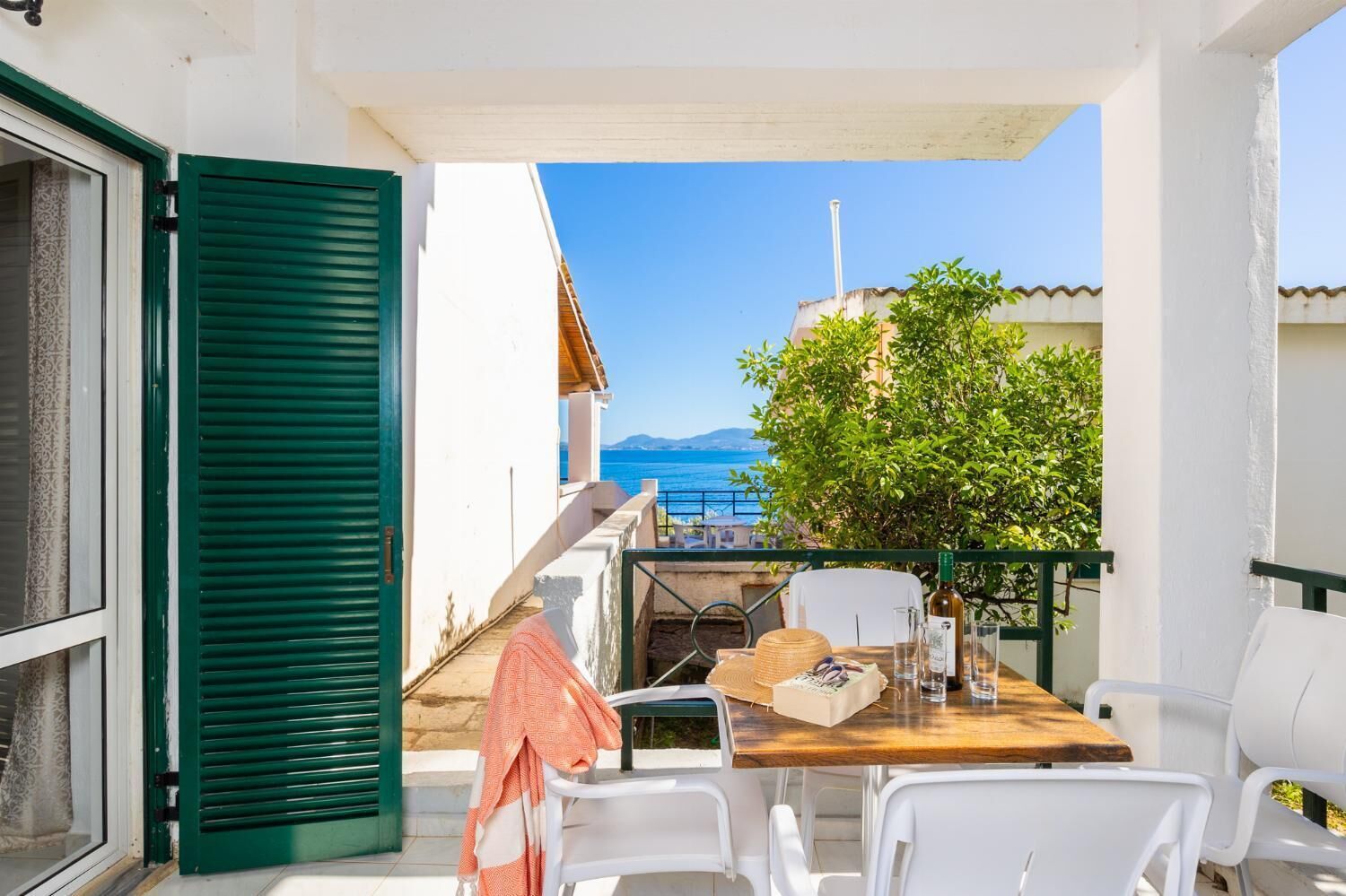 A balcony with a wooden table, white chairs, and a view of the sea.