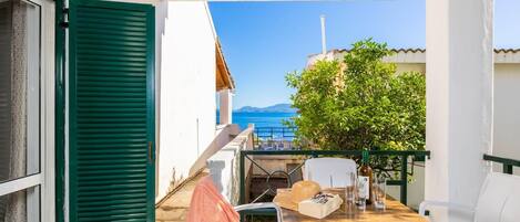 A balcony with a wooden table, white chairs, and a view of the sea.